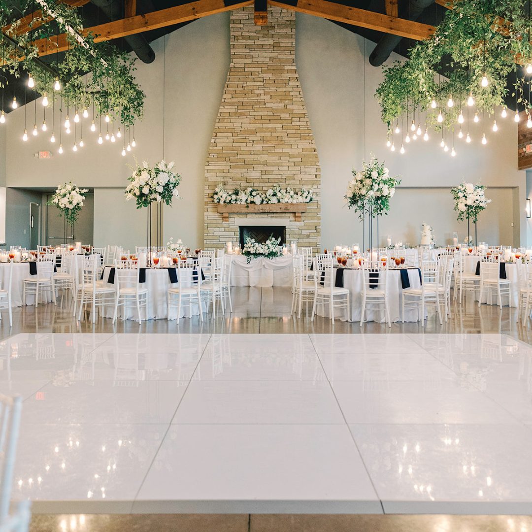 Glossy white dance floor in a wedding reception hall with white chairs and floral centerpieces